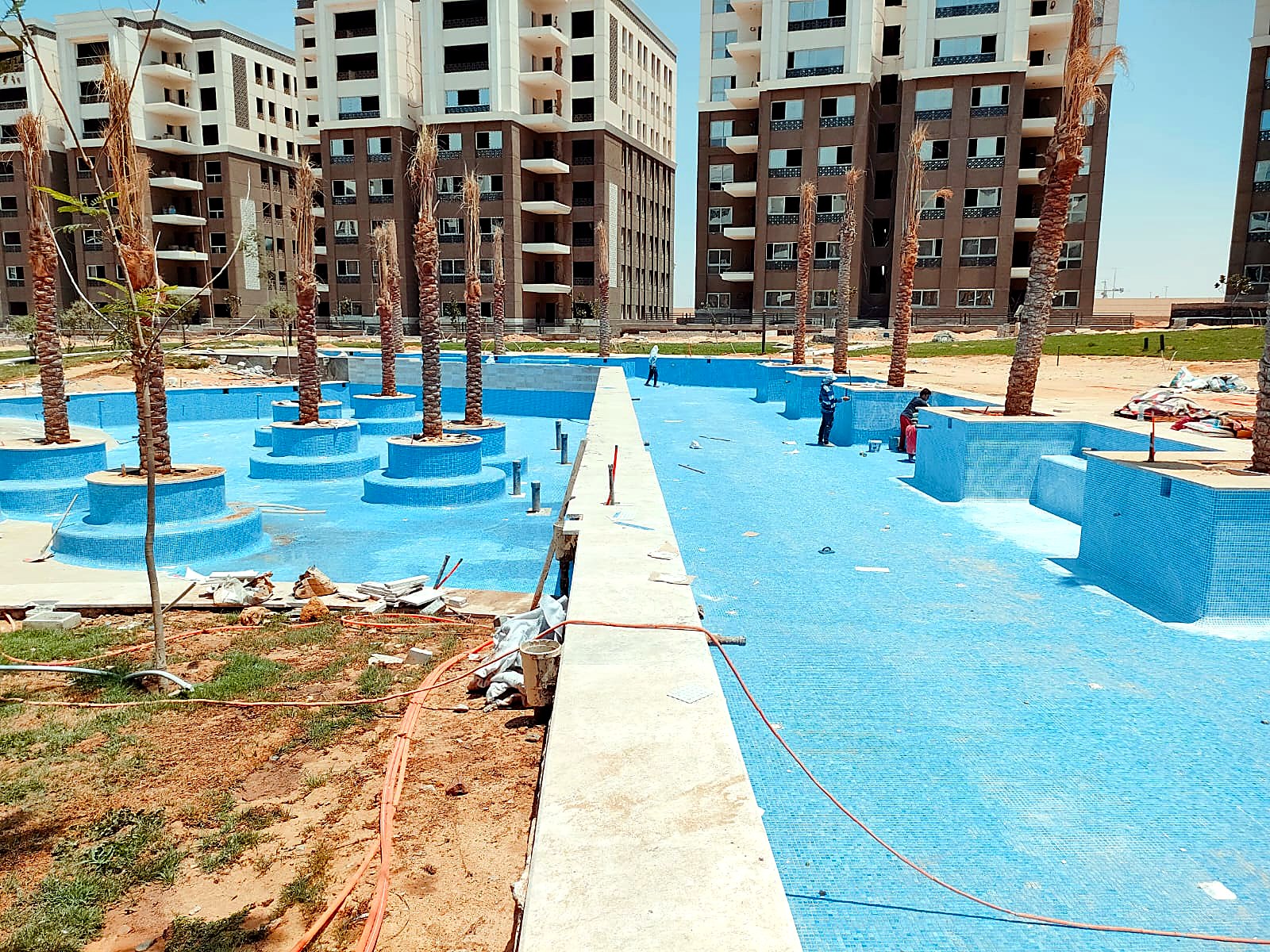 Compound pool with crews installing blue tiles